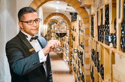 Ein Kellner hat ein Glas Rotwein in der Hand im Weinkeller des Sterne Restaurants Baiersbronn