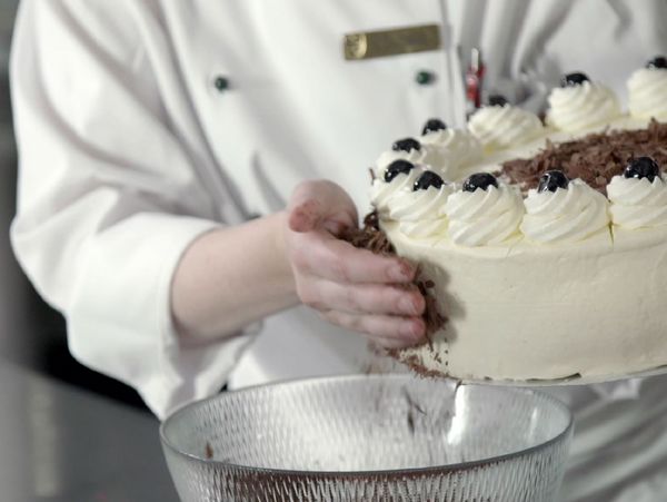 Nahaufnahme eines Konditors beim verzieren einer Torte