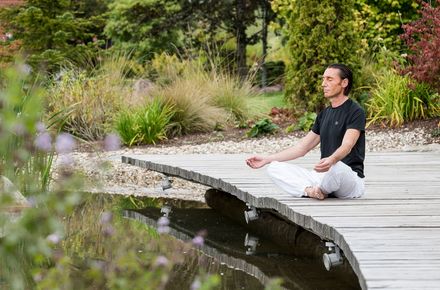 Ein Mann sitzt auf einem Holzsteg und meditiert im Luxushotel Schwarzwald
