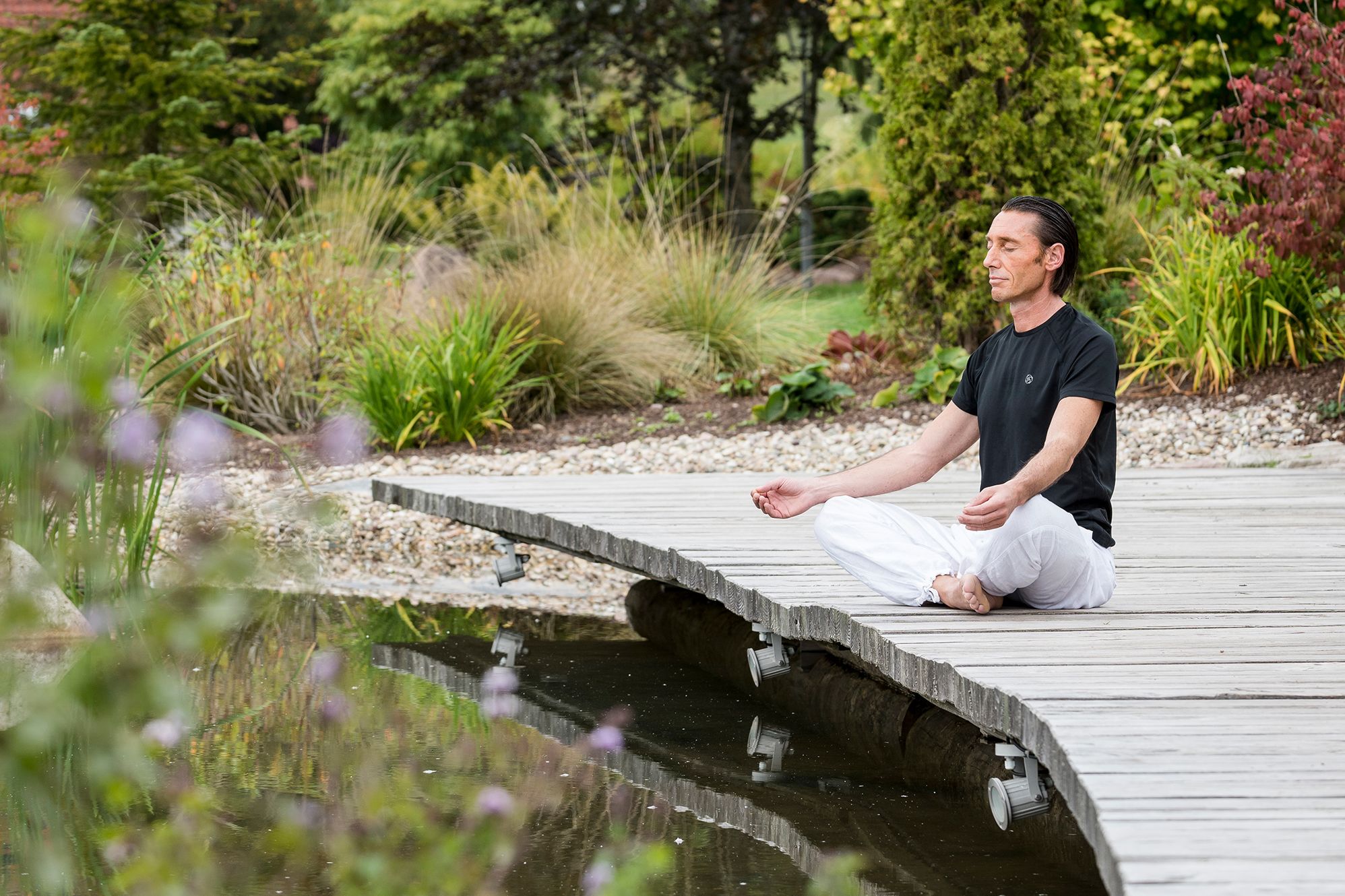 Ein Mann sitzt auf einem Holzsteg und meditiert im Luxushotel Schwarzwald