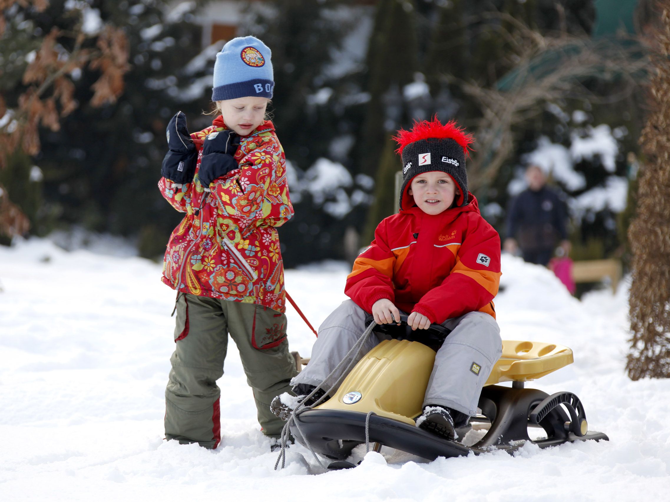 Zwei Kinder spielen mit einem Schlitten im Schnee während ihres Winterurlaubs im Schwarzwald