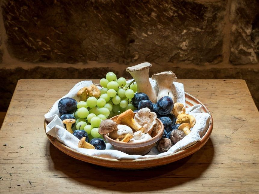 Detailaufnahme von Trauben, Pflaumen und Pilzen in einer Holzschale