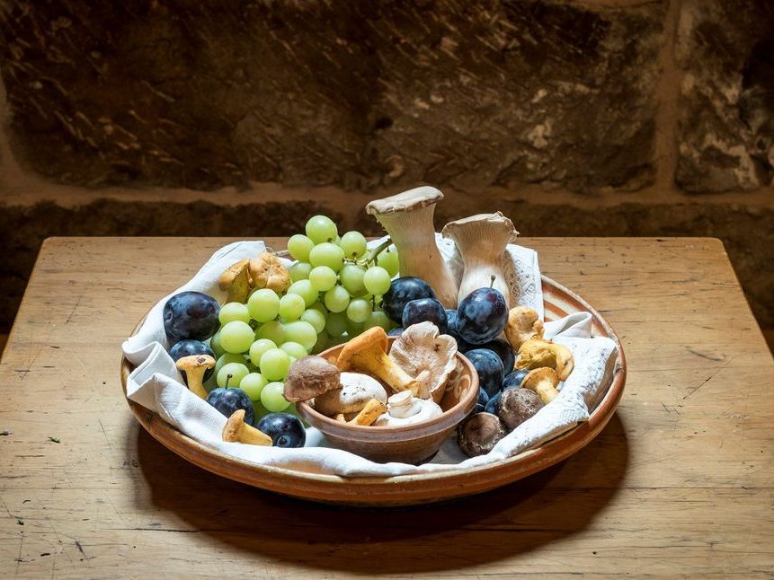 Detailaufnahme von Trauben, Pflaumen und Pilzen in einer Holzschale