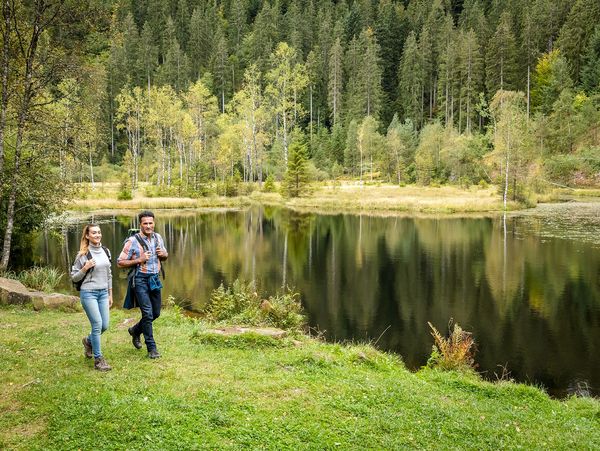 Zwei Wanderer spazieren entlang eines Sees inmitten der grünen Wälder im Schwarzwald
