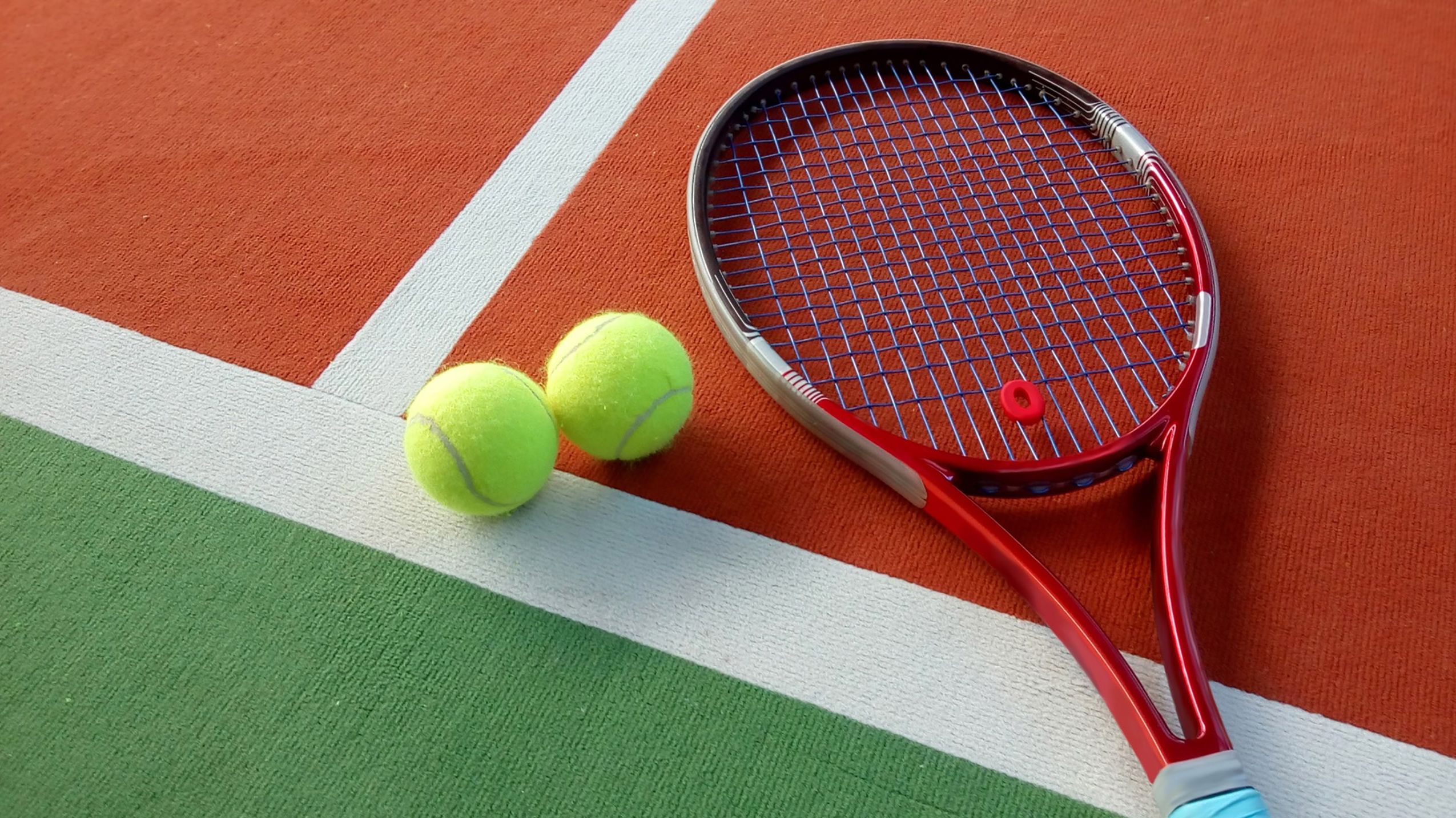 Detailaufnahme eines Tennisschlägers und zwei Tennisbällen auf dem Boden eines Hallenplatzes für einen Winterurlaub im Schwarzwald