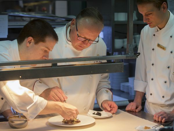 Drei Köche in Kochuniform stehen in einer Küche und dekorieren Häppchen