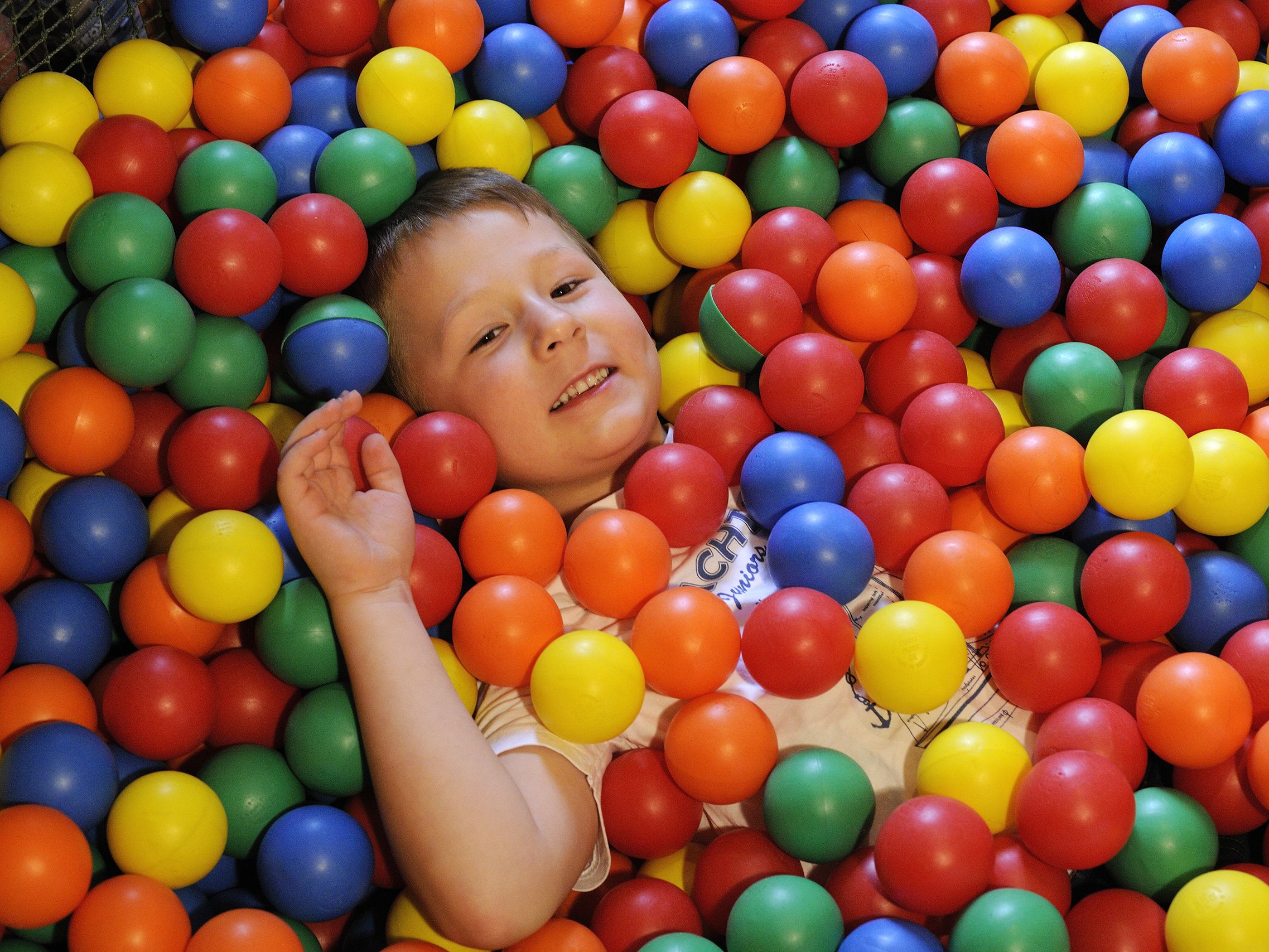Aufnahme eines kleinen Jungen der in einem bunten Bällebad liegt