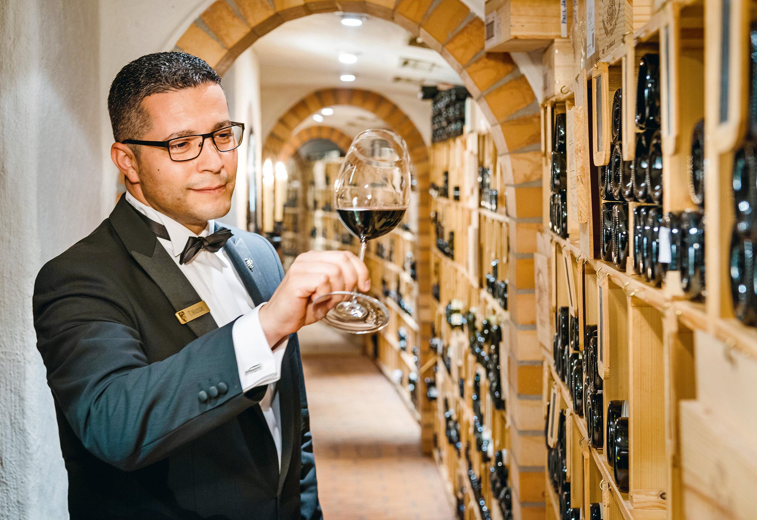 Ein Kellner hat ein Glas Rotwein in der Hand im Weinkeller des Sterne Restaurants Baiersbronn
